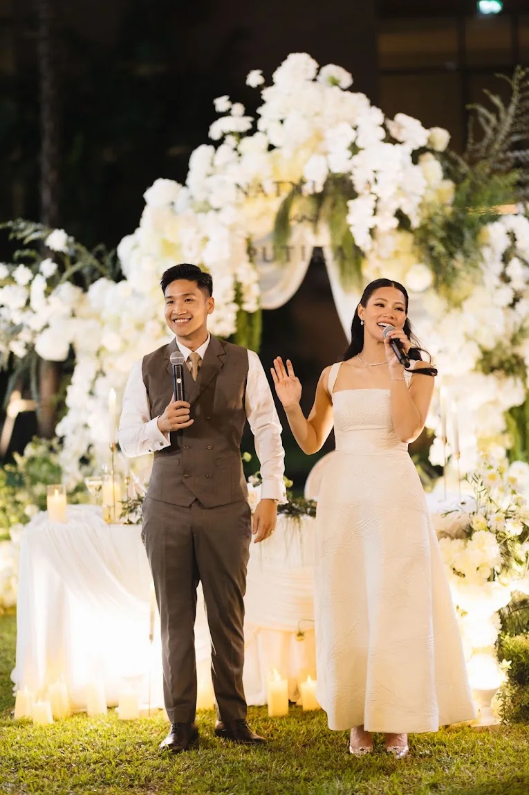 Couple speaking at the outdoor floral stage at the Annie & Louis celebration in Bangkok