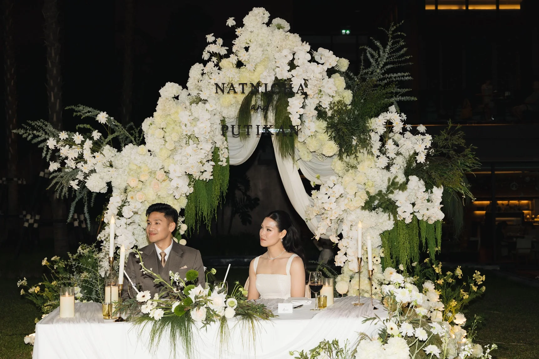 Couple seated behind the white floral sweetheart table at the Annie & Louis celebration in Bangkok