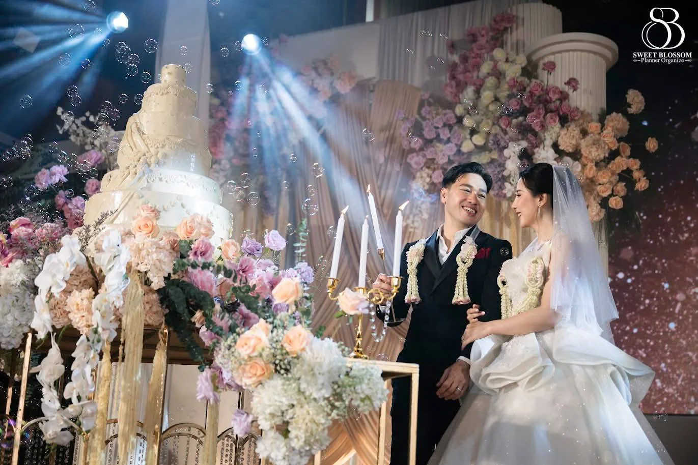 Couple beside the cake and floral stage at the Foam & Petch celebration in Lopburi