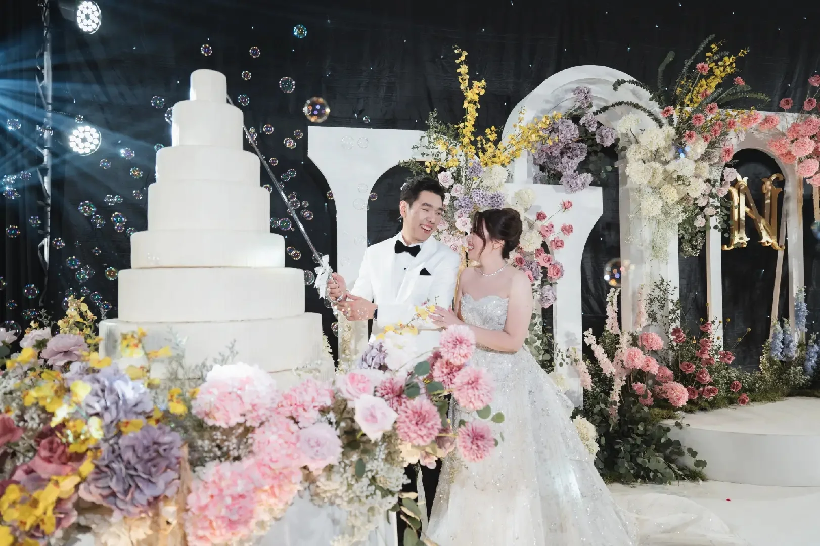 Couple beside the wedding cake and floral stage at the Jum & Jai celebration in Chonburi