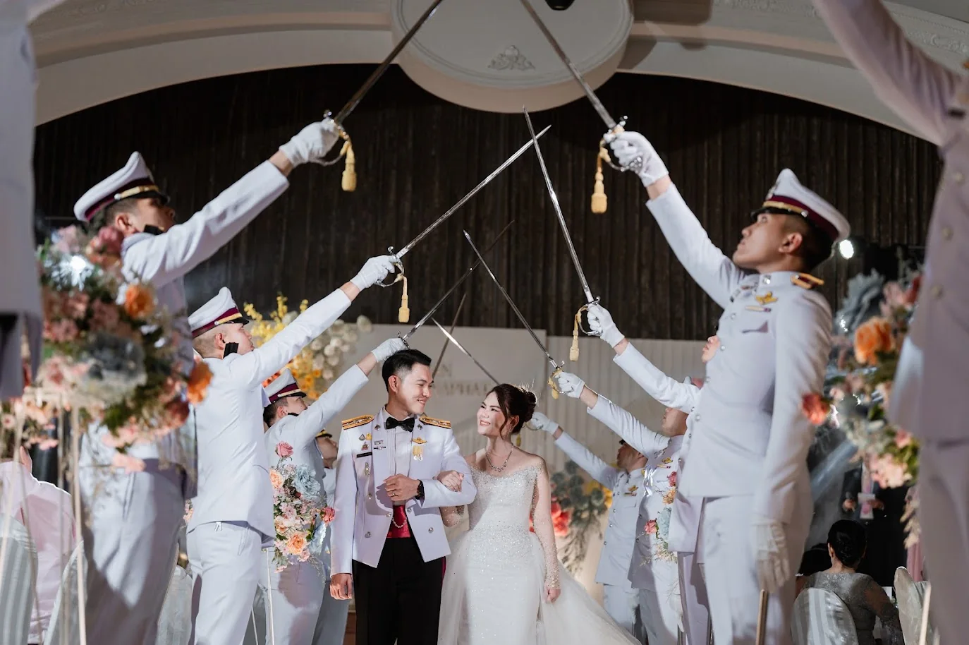 Couple walking beneath the ceremonial sword arch at the Koko & Raam celebration in Chonburi