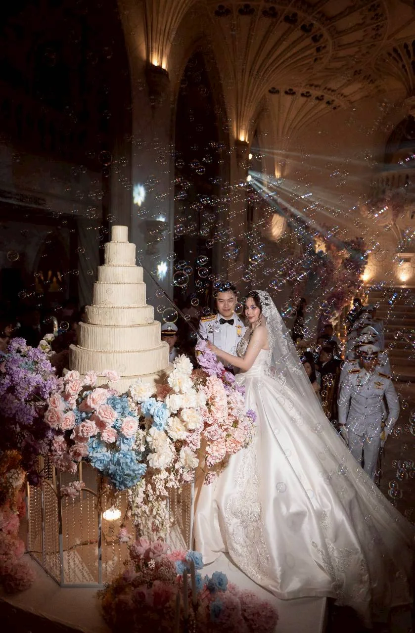 Couple beside the wedding cake and pastel flowers at the Nan & Big celebration in Bangkok