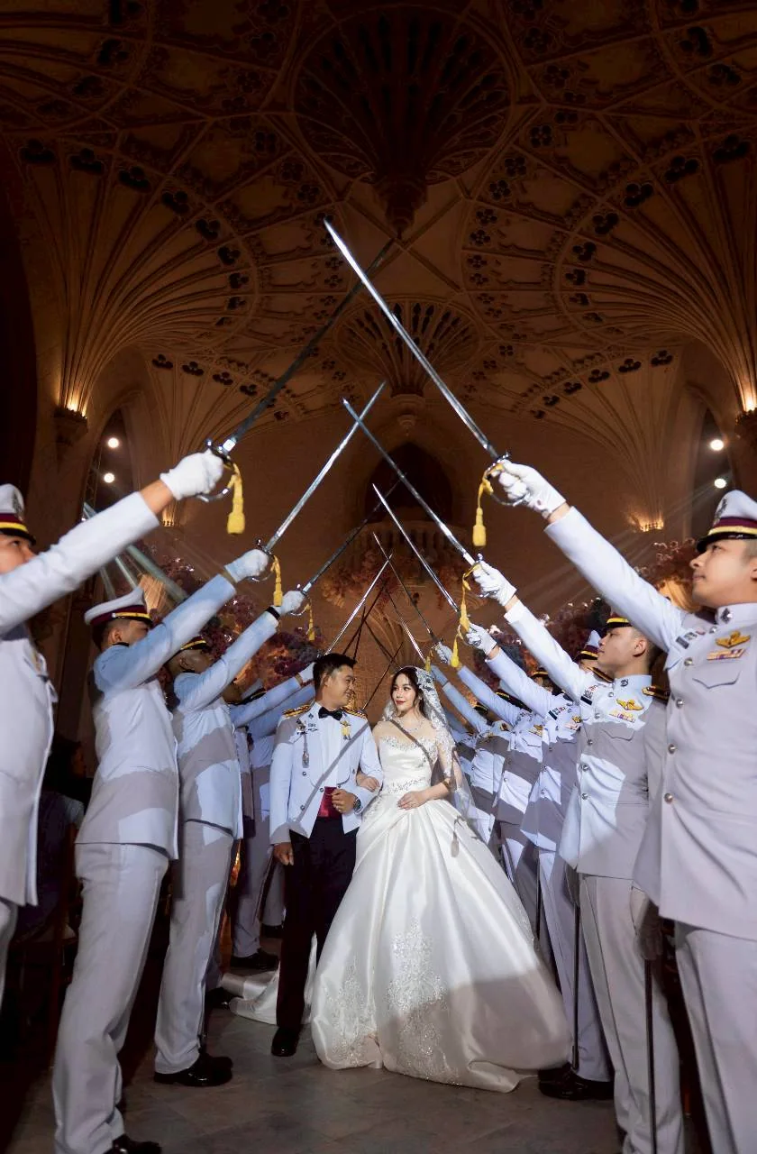 Couple walking beneath crossed ceremonial swords at the Nan & Big celebration in Bangkok