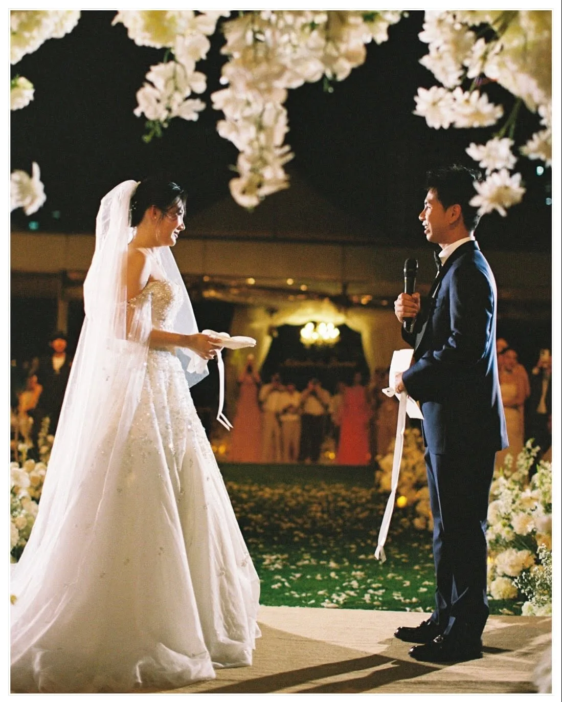 Couple facing each other beneath the floral arch at the Natt & Yang celebration in Bangkok