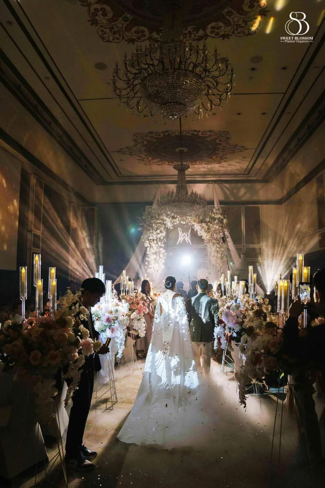 Couple walking through a candlelit floral aisle at the Risa & Ong celebration in Bangkok