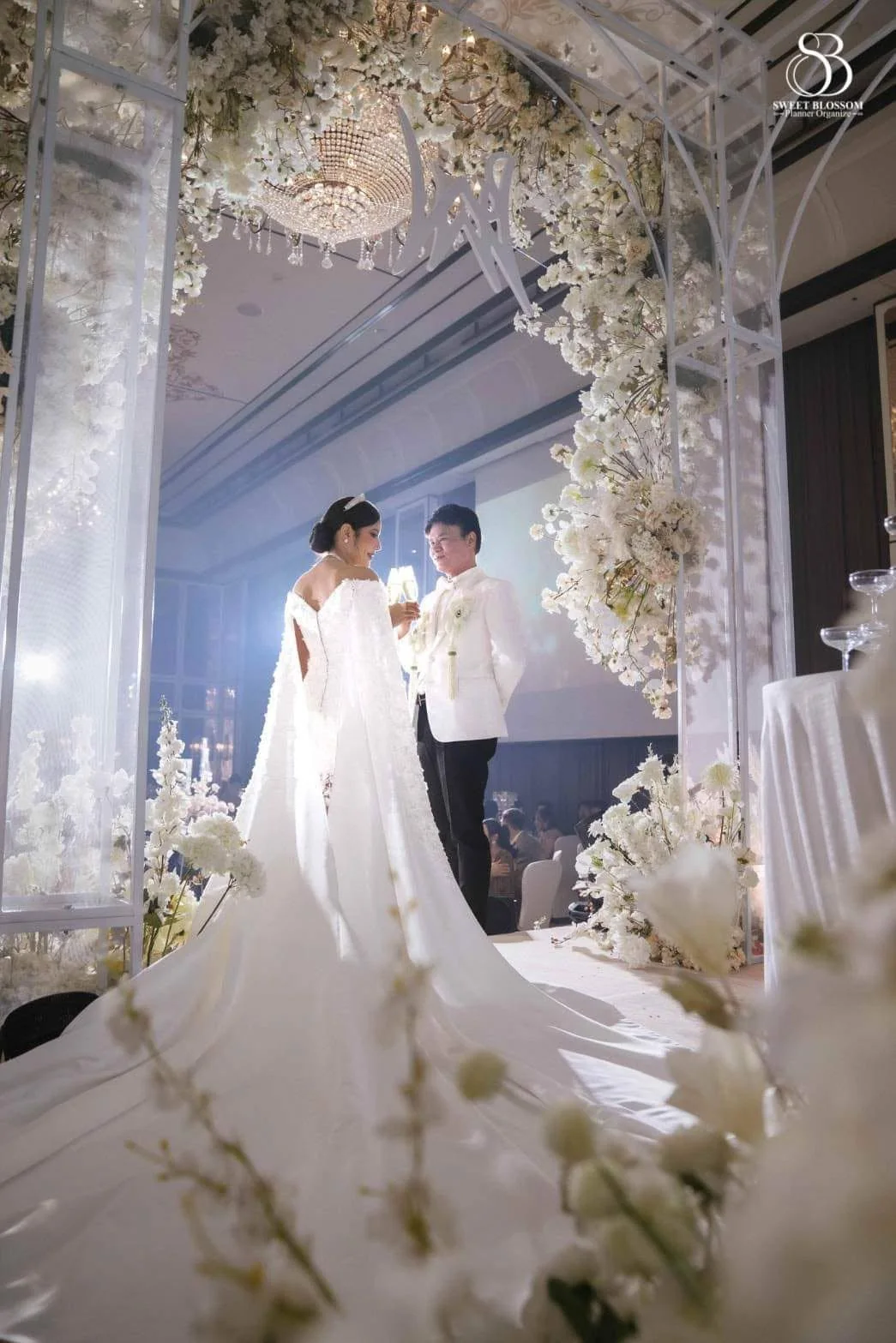 Bride and groom beneath a white floral arch at the Risa & Ong celebration in Bangkok