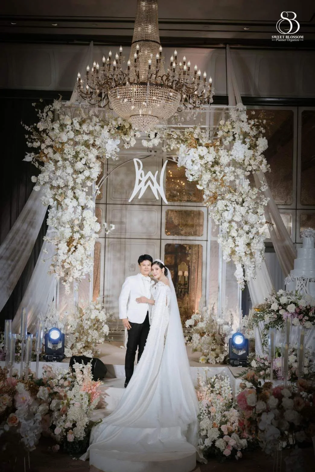 Bride and groom on the chandelier ballroom stage at the Risa & Ong celebration in Bangkok