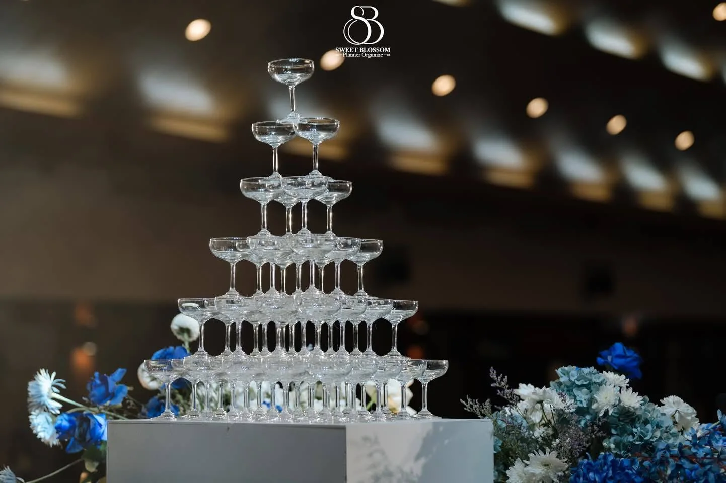 Champagne tower framed by blue flowers at the Yam & Ball celebration in Lopburi